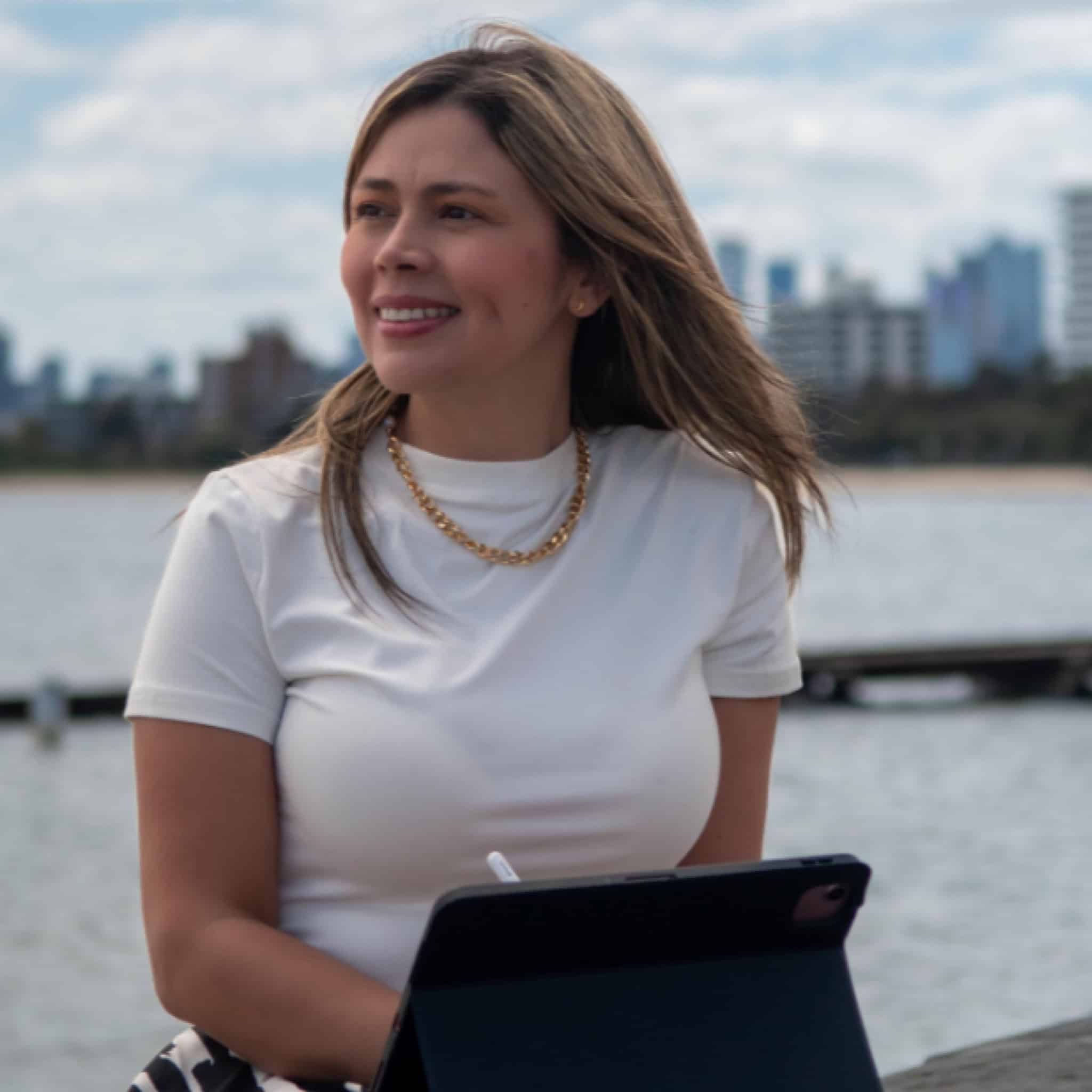 Cristina Carvajal sonriendo junto al río con ciudad de fondo.