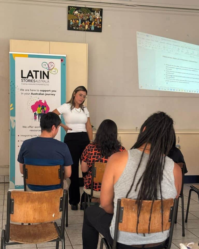 Conferencia sobre historias latinas en Australia, con una presentadora explicando a un grupo de asis.