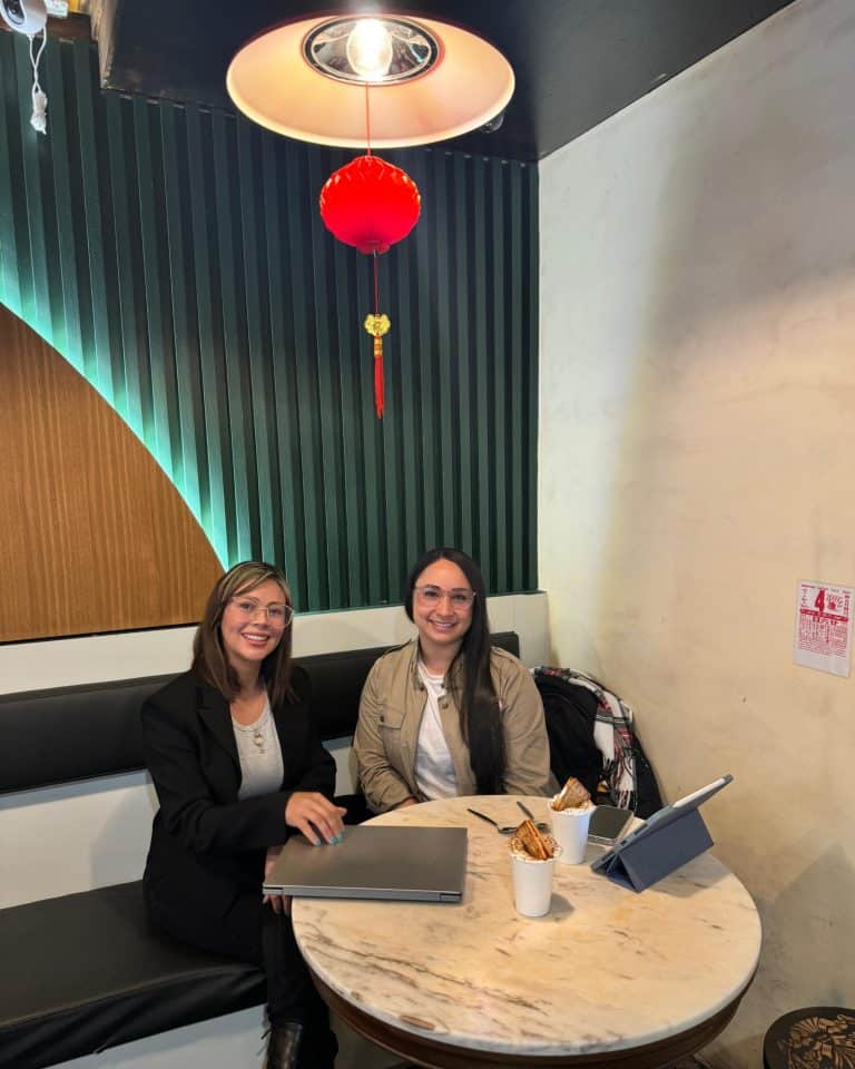 Imagen de Cristina Carvajal y otra mujer en una cafetería, sonriendo y trabajando juntas.