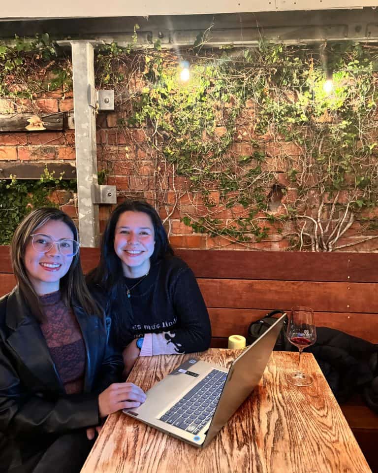 Cristina Carvajal sonriendo en un restaurante con laptop y copa de vino.