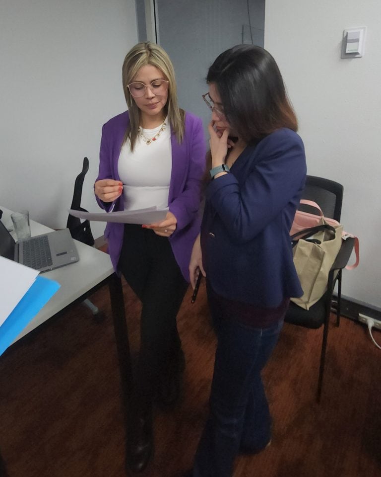 Dos mujeres profesionales discutiendo documentos en oficina moderna.