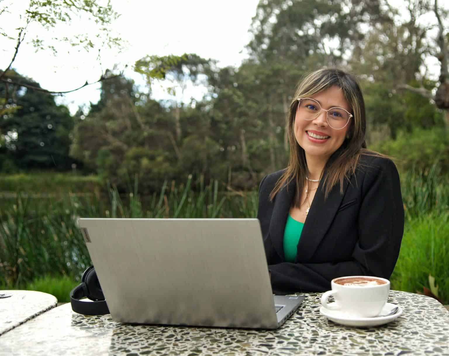 Cristina Carvajal trabajando en un entorno natural con laptop y taza de café.